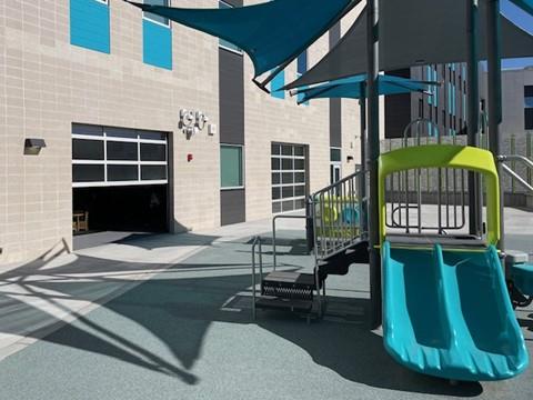 Outdoor school courtyard with play structure connected to classrooms via glass doors